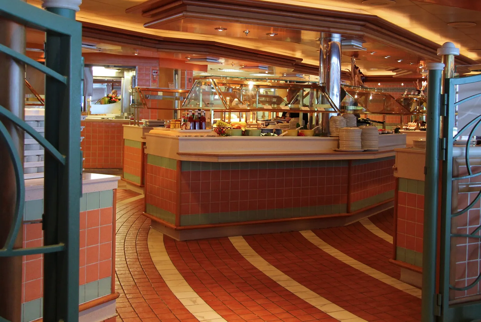 A cruise ship buffet counter with stacks of plates, the kind of crew work the daily gratuity pays for