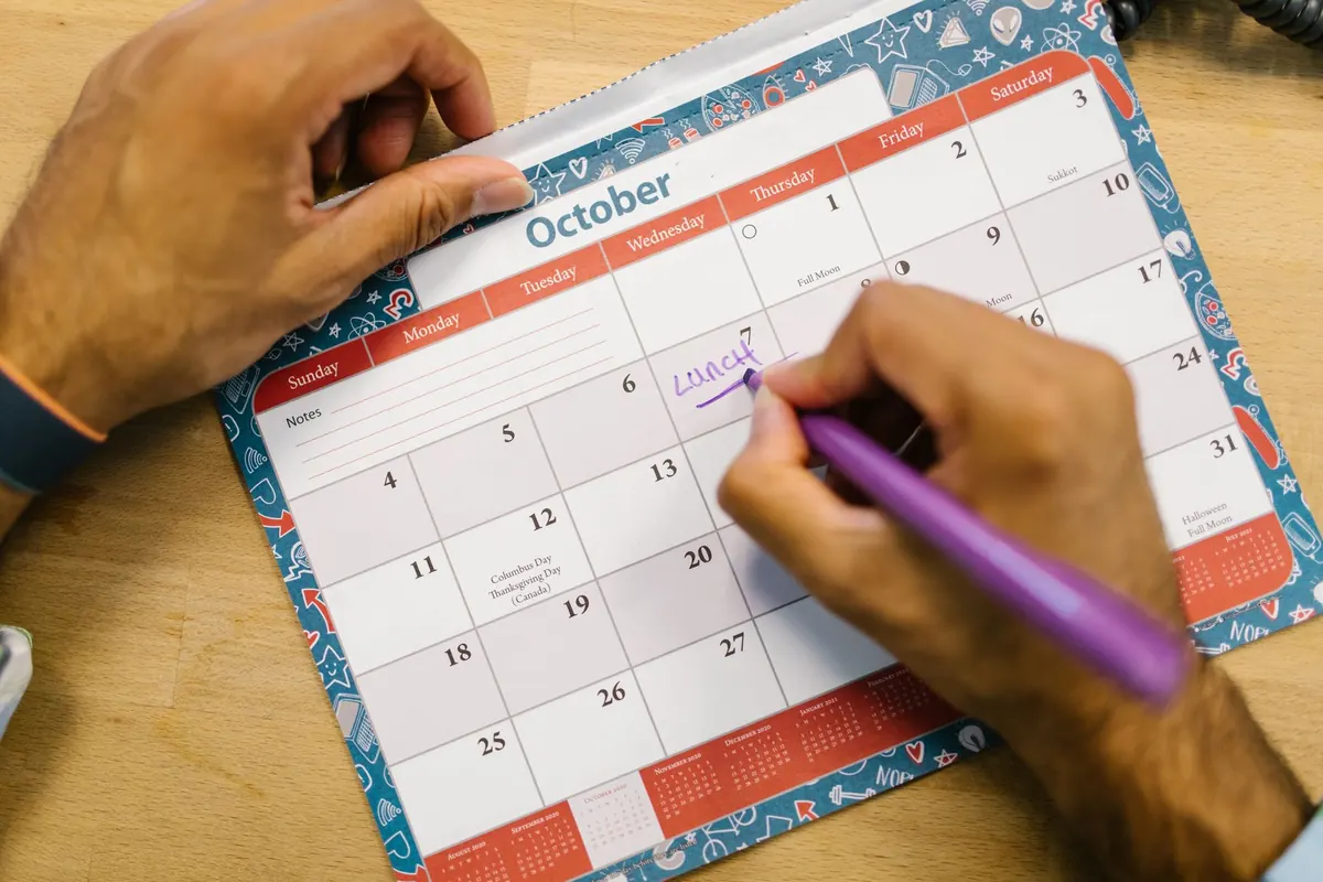 A hand writing a note on a paper calendar page for October