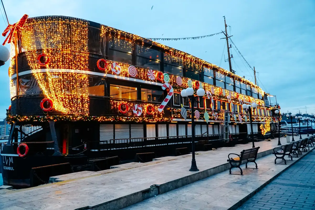 A ship at the quay covered in holiday lights and candy cane decorations at dusk
