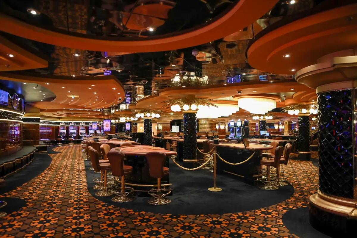 A casino floor with card tables and slot machines under warm light, where Club Royale offers are earned
