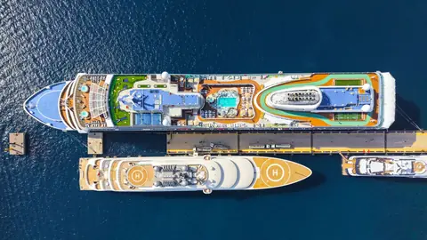 Two cruise ships seen from above at a pier, pools and decks laid out in the sun